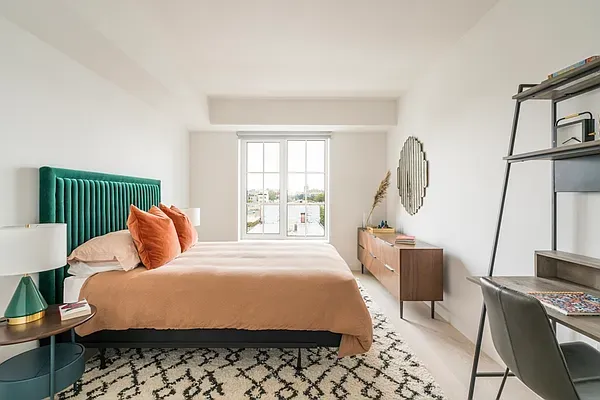 a bedroom with a bed a mirror on dresser and a window