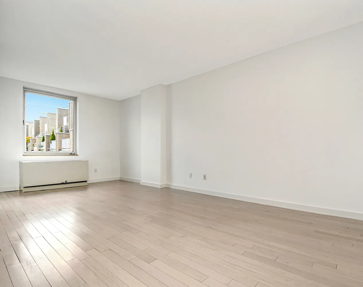 a view of an empty room with a window and wooden floor