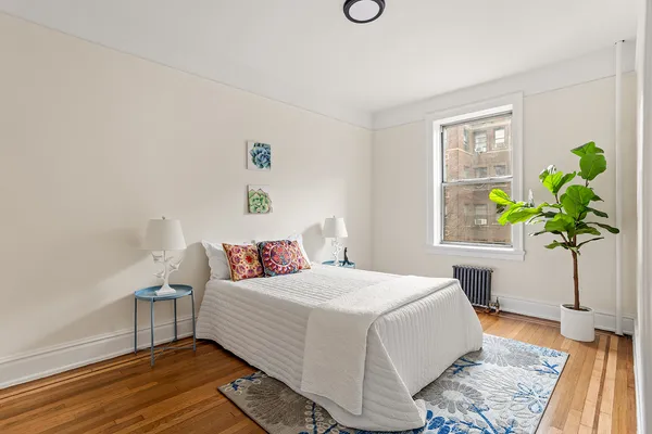 a bedroom with a bed a dresser and potted plant