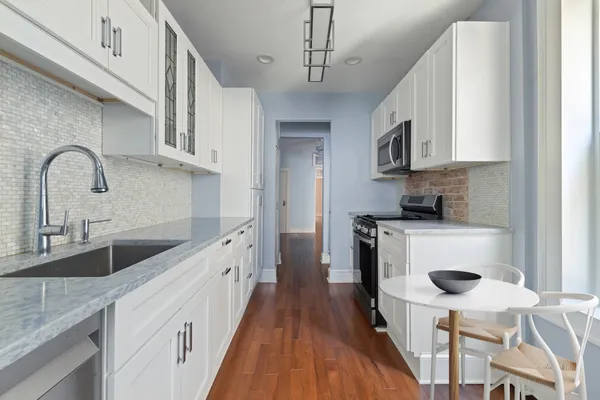 a kitchen with stainless steel appliances granite countertop a white stove top oven a sink a refrigerator and white cabinets with wooden floor
