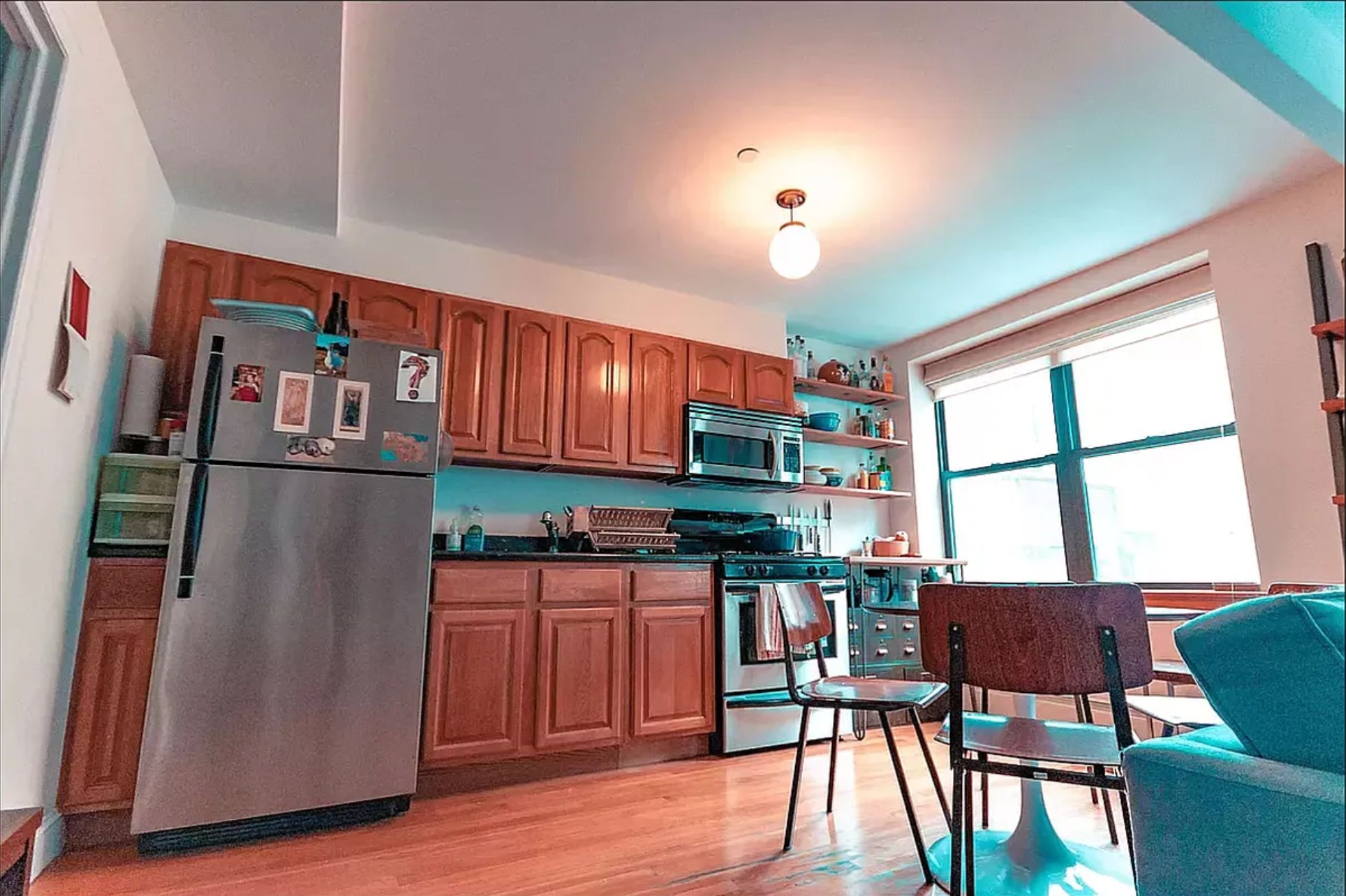 133 Essex Street, Unit 403 Manhattan, NY 10002 - Photo 2 of 7 a kitchen with stainless steel appliances granite countertop a refrigerator a stove top oven a dining table and chairs with wooden floor