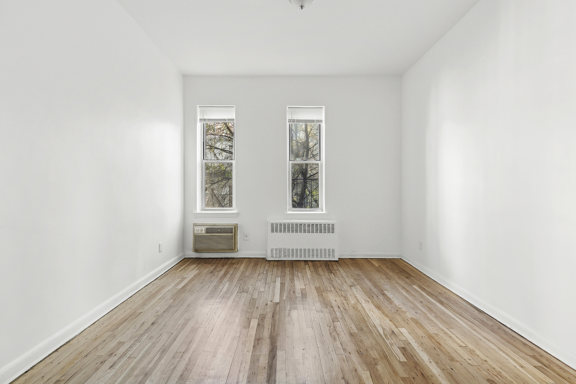 313 East 89th Street, Unit 4F Manhattan, NY 10128 - Photo 3 of 5 an empty room with wooden floor and windows