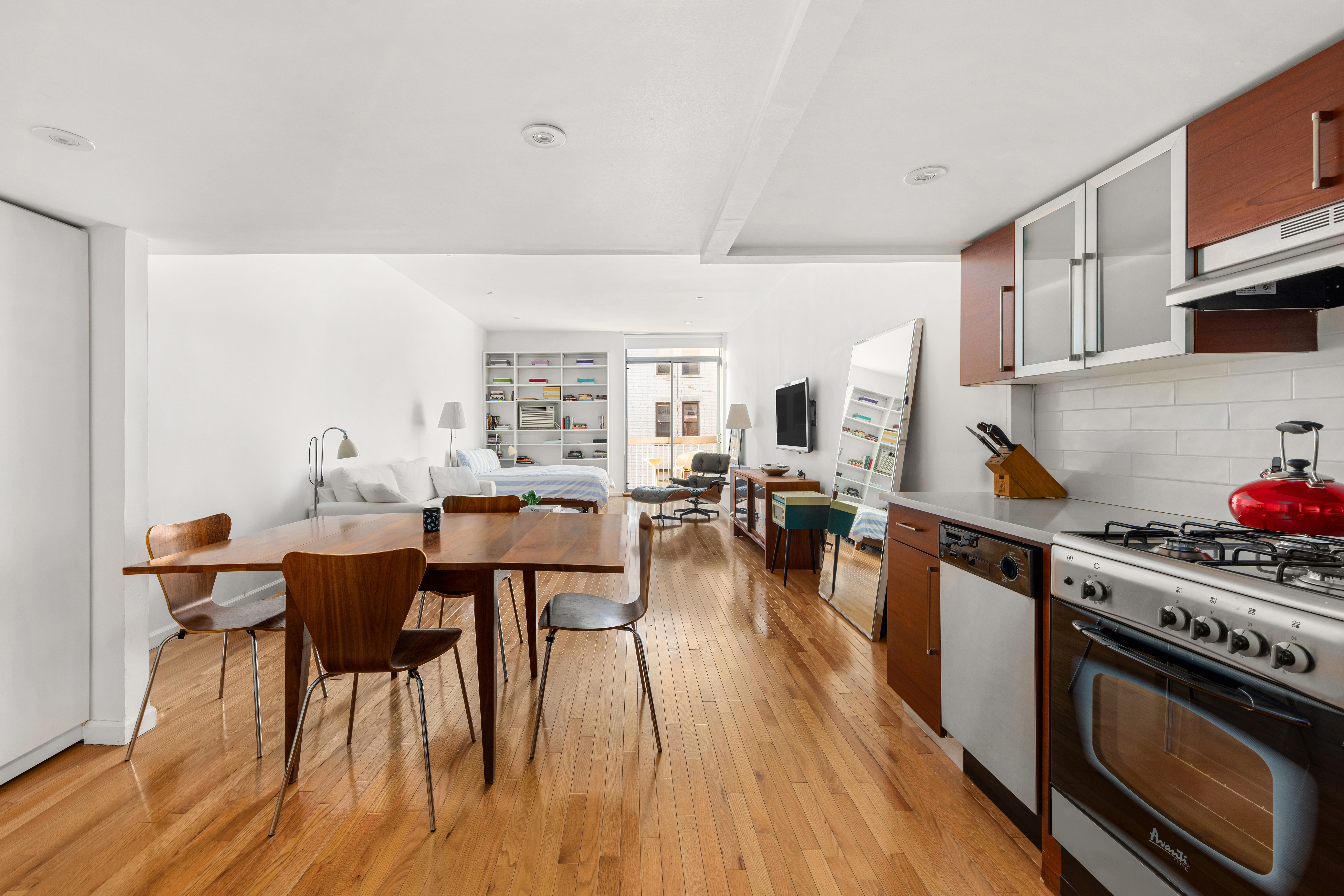 184 Thompson Street, Unit 4E Manhattan, NY 10012 - Photo 2 of 10 a kitchen with stainless steel appliances a dining table chairs stove and white cabinets
