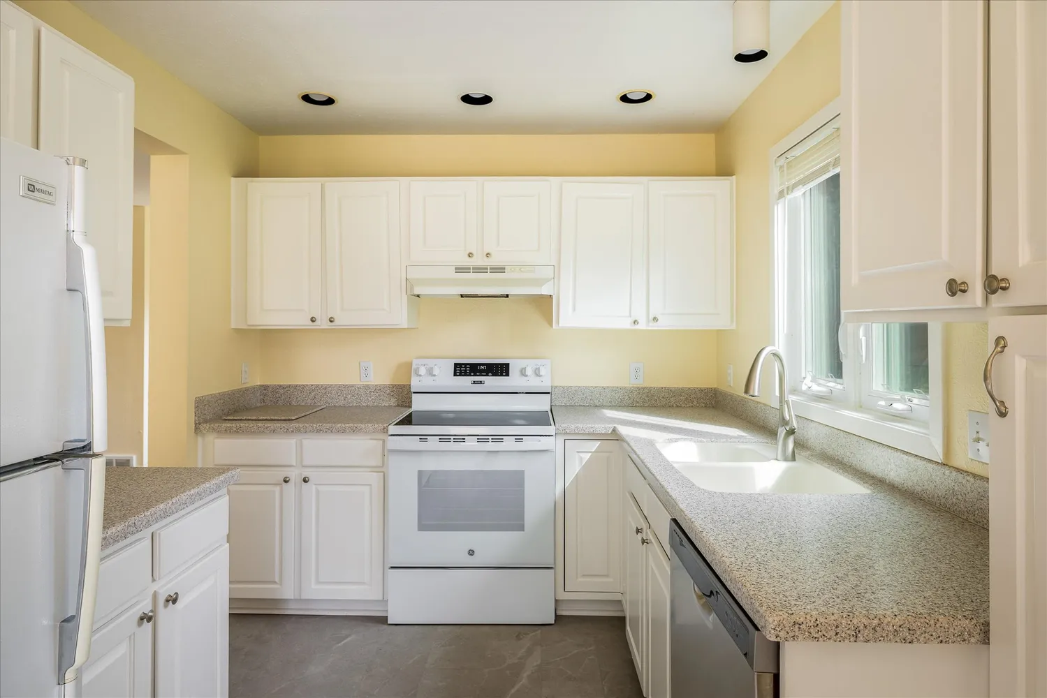 a kitchen with white cabinets appliances a sink and a window