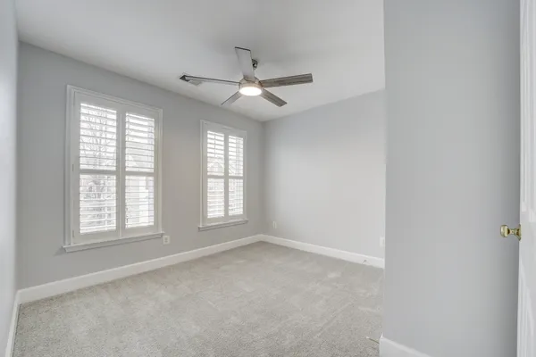 an empty room with chandelier fan and windows