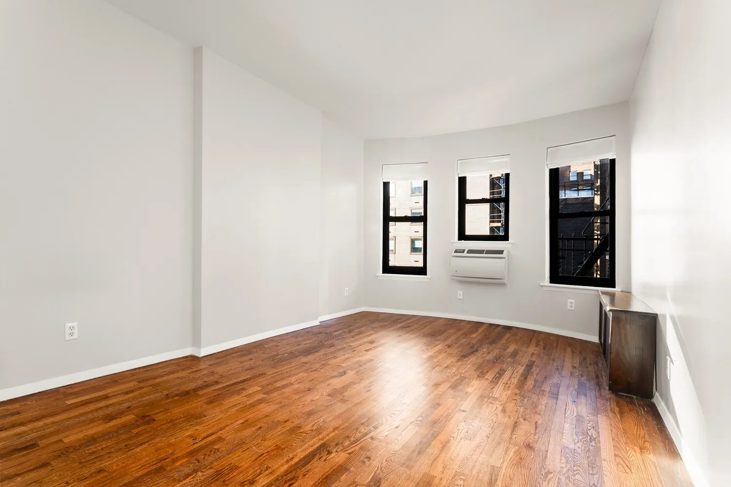 a view of an empty room with window and wooden floor