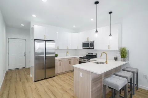 a kitchen with stainless steel appliances kitchen island granite countertop a refrigerator a sink a stove and white cabinets with wooden floor