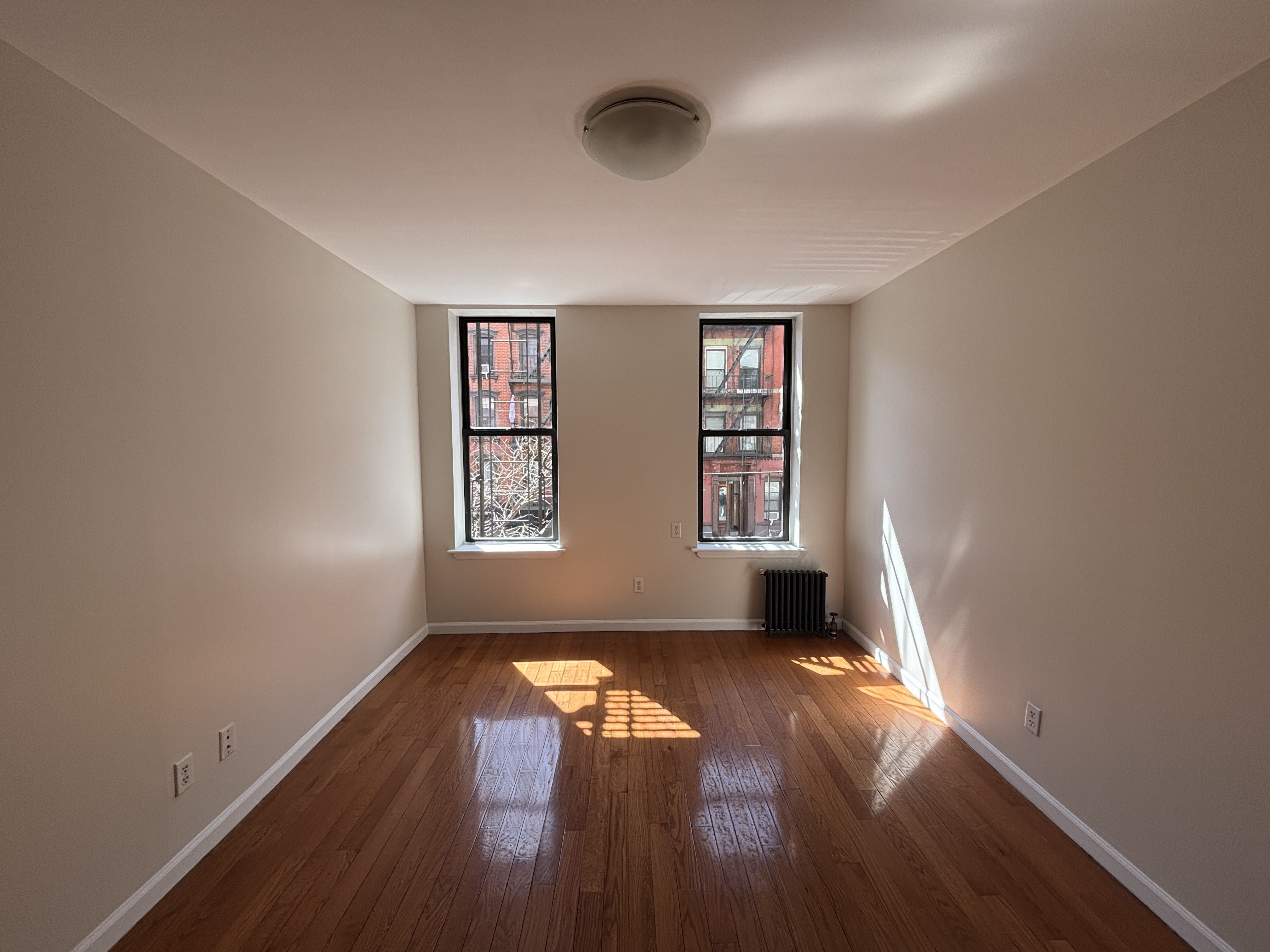 99 St Marks Place, Unit 4B Manhattan, NY 10009 - Photo 1 of 10 an empty room with wooden floor and windows