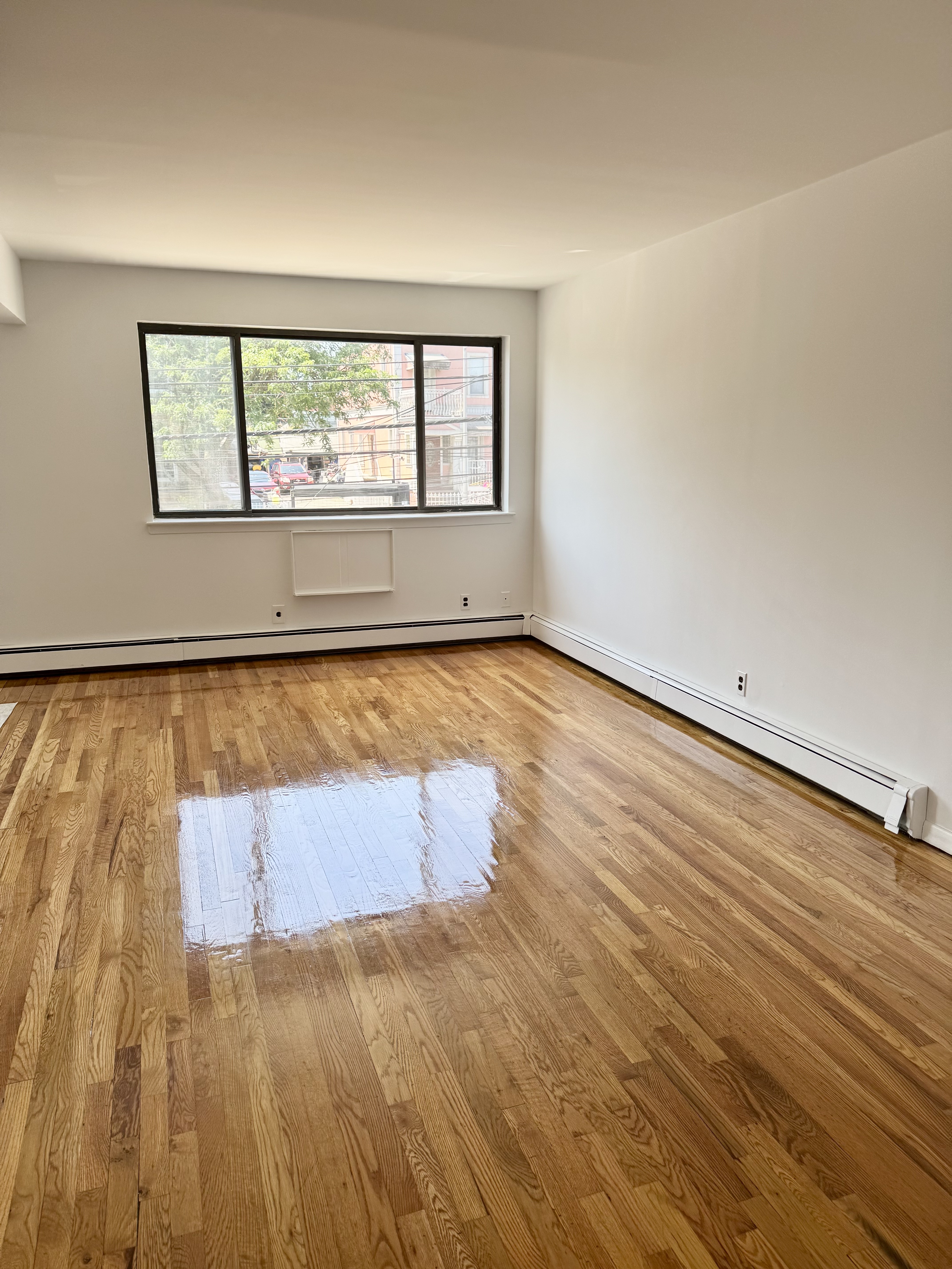 59-15 39th Avenue, Unit 2 Queens, NY 11377 - Photo 3 of 13 an empty room with wooden floor and windows