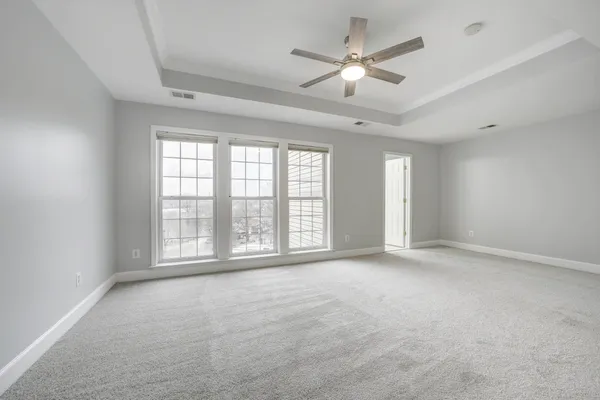 an empty room with chandelier fan and windows