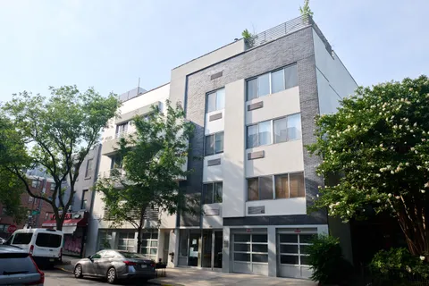 a front view of a building with a garden and trees