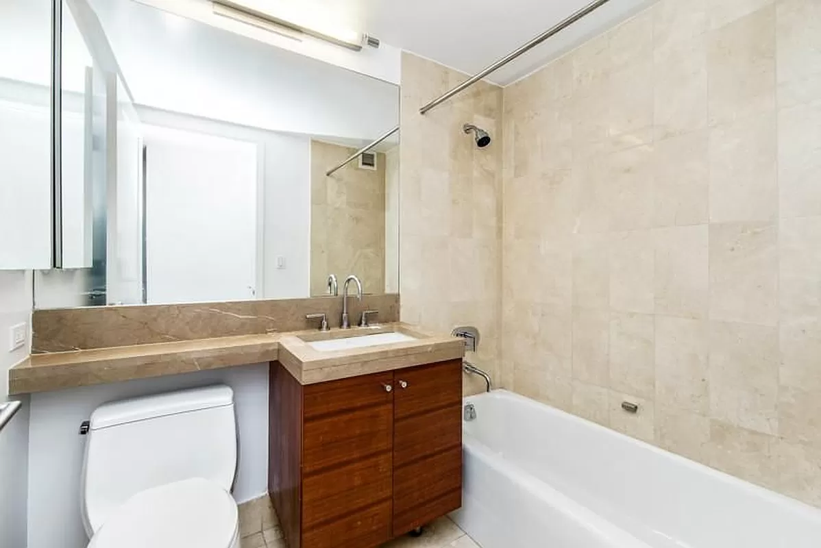 30 West Street, Unit 6B Manhattan, NY 10004 - Photo 10 of 13 a bathroom with a granite countertop sink a mirror a bathtub and shower
