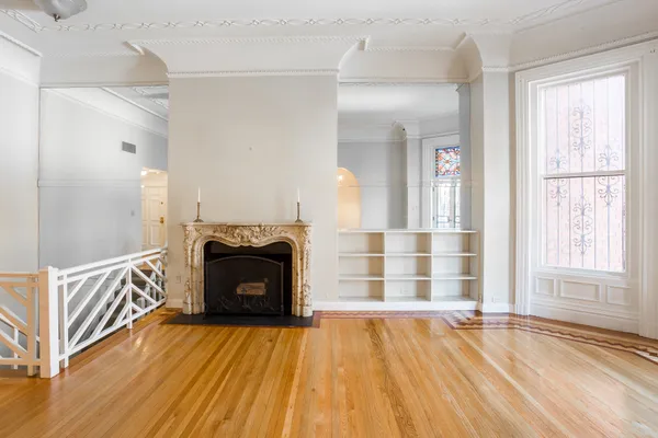 a view of an empty room with wooden floor fireplace and a window