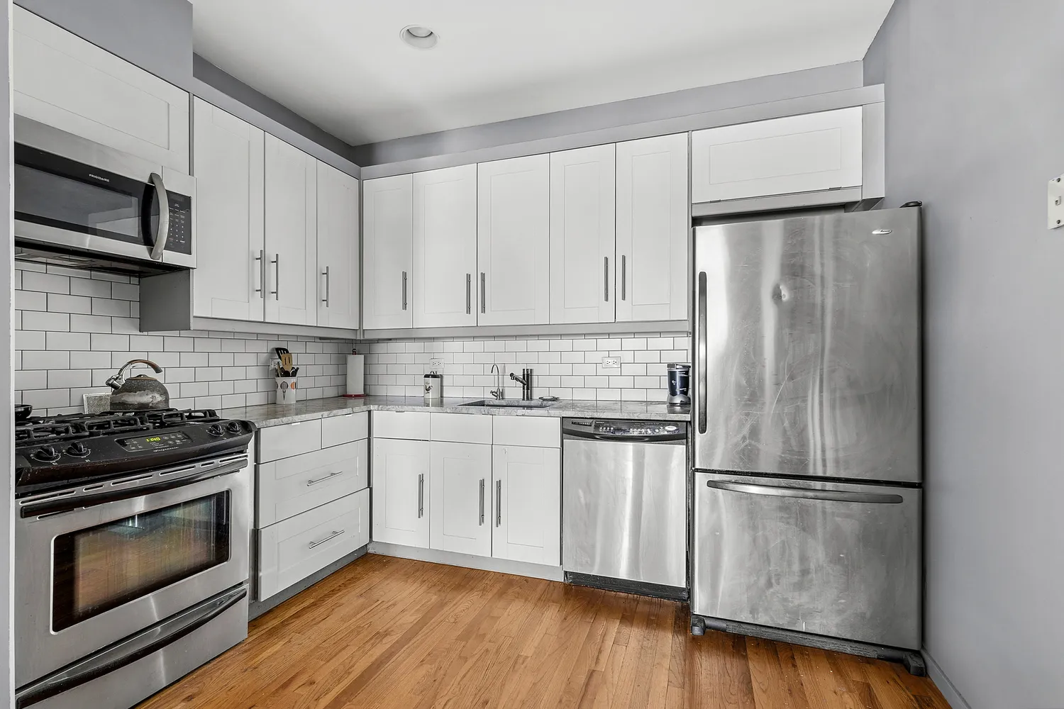 a kitchen with granite countertop white cabinets stainless steel appliances and wooden floor
