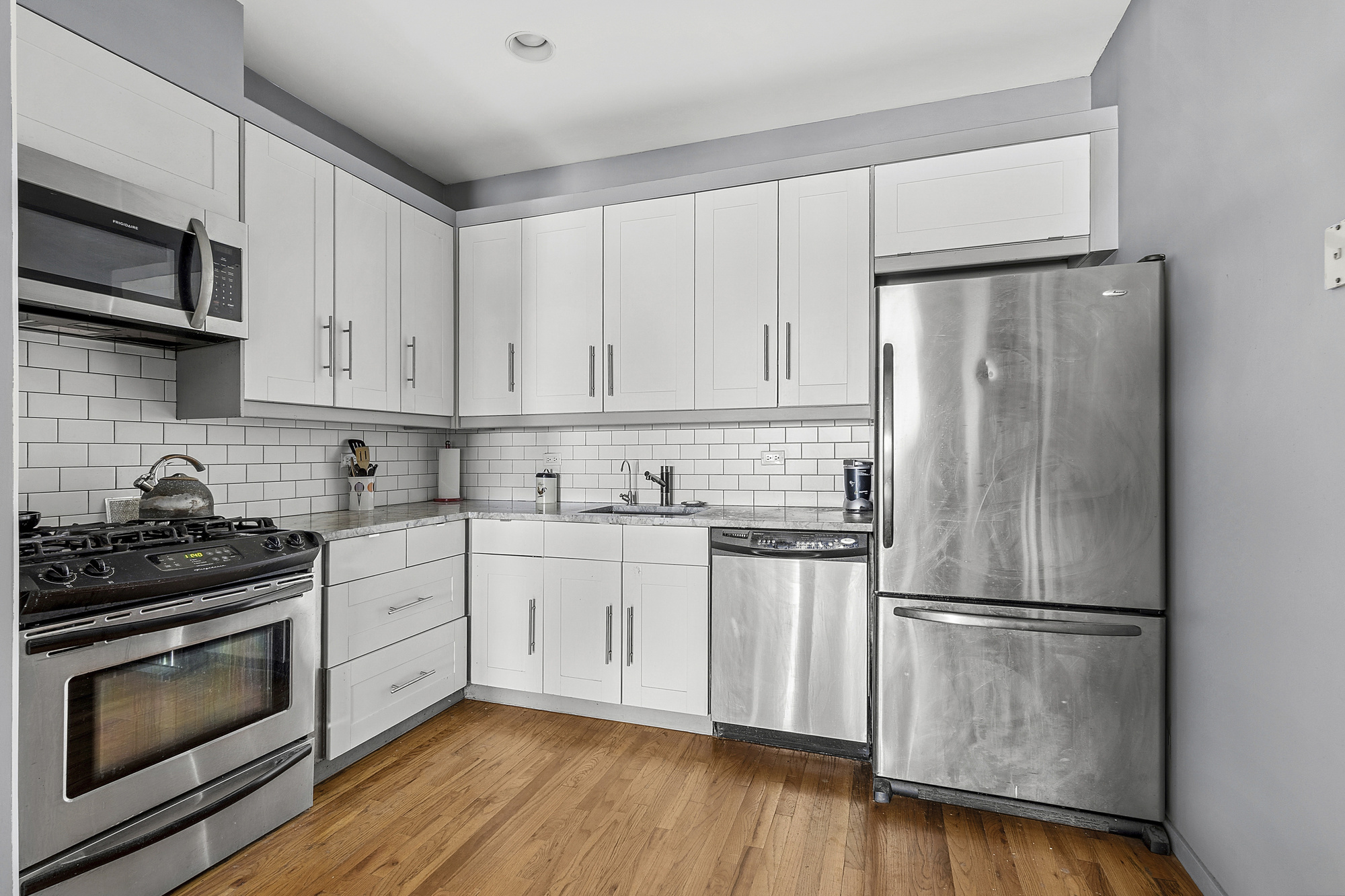 14-25 Broadway, Unit 5R Queens, NY 11106 - Photo 3 of 5 a kitchen with granite countertop white cabinets stainless steel appliances and wooden floor