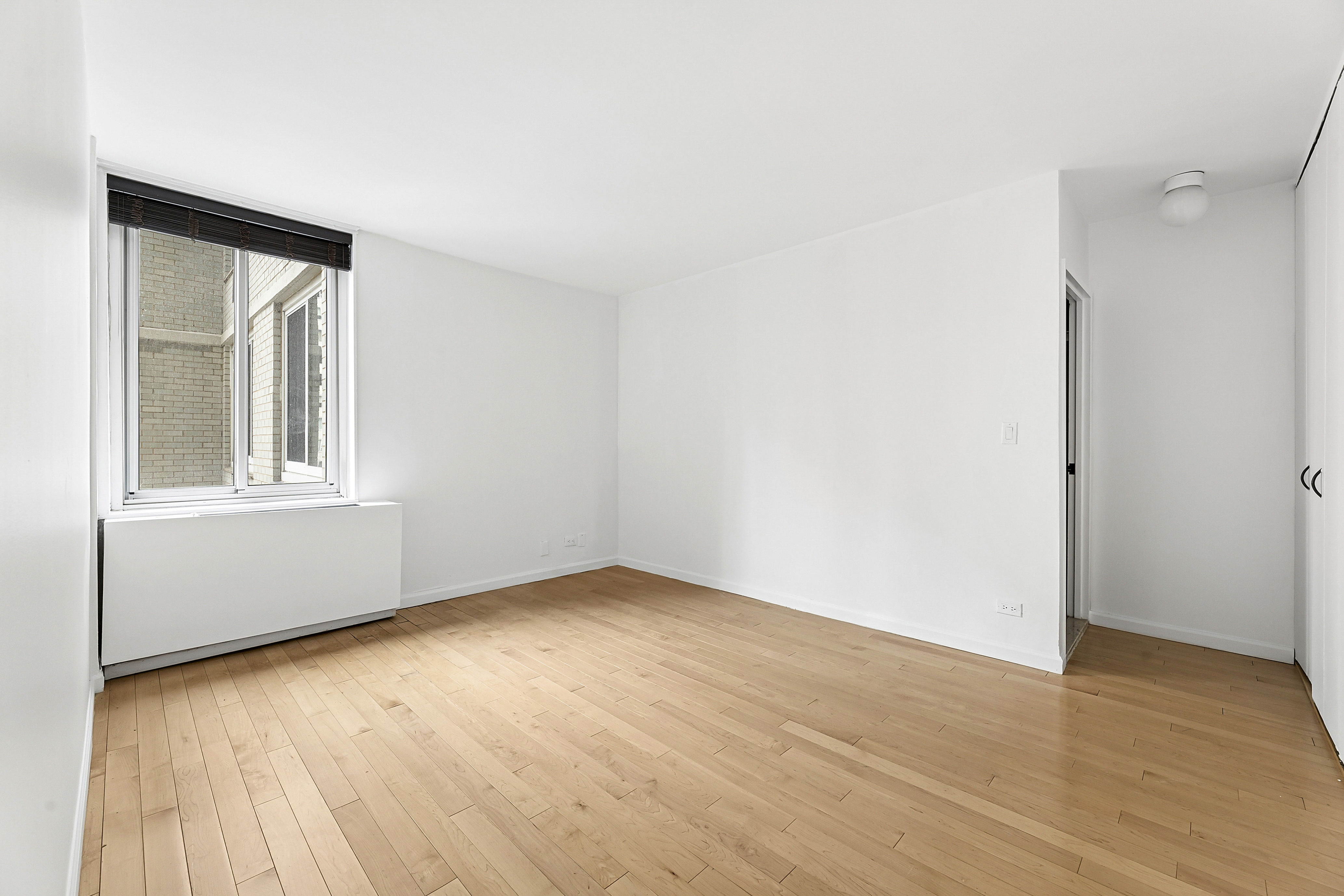 220 East 65th Street, Unit 8J Manhattan, NY 10065 - Photo 5 of 13 a view of an empty room with wooden floor and a window