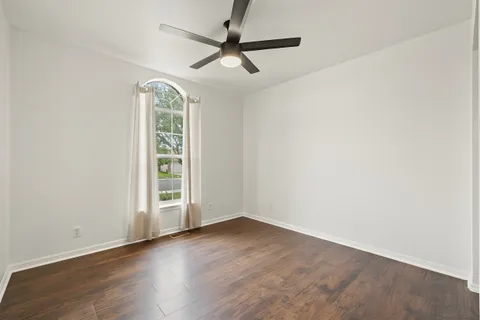 an empty room with wooden floor fan and windows