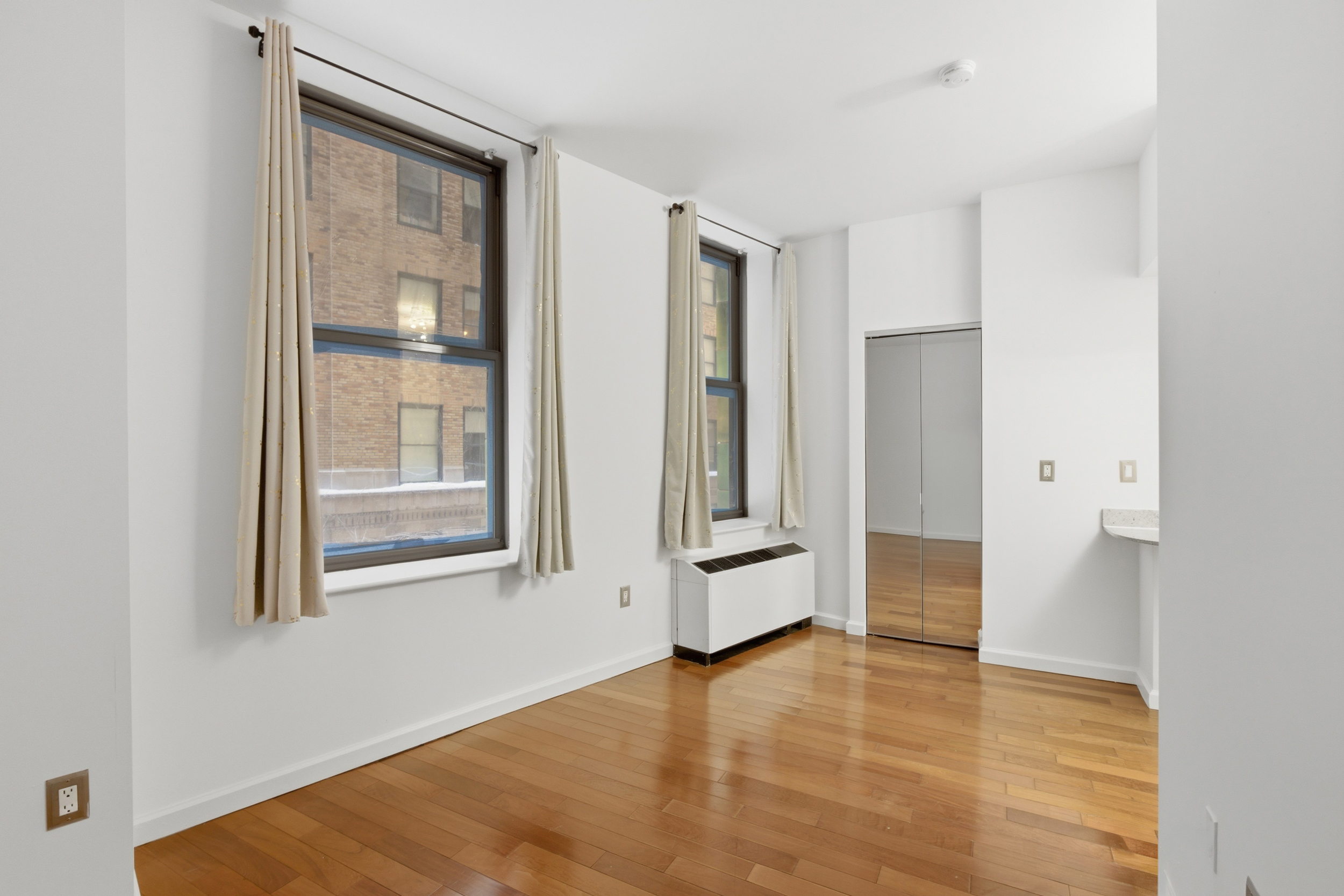 1 Wall Street Court, Unit 406 Manhattan, NY 10005 - Photo 2 of 7 a view of an empty room with wooden floor and a window