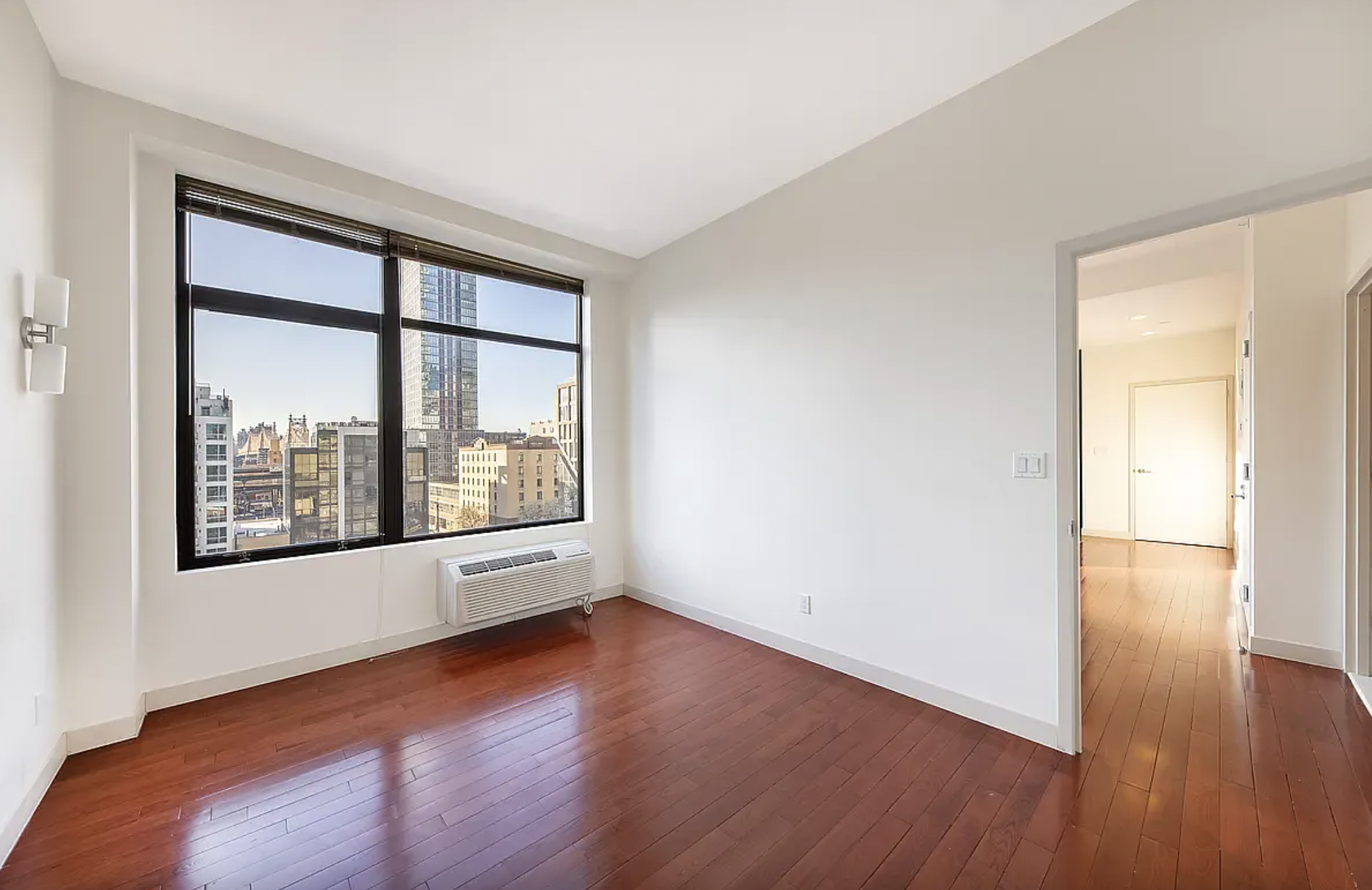 42-37 27th Street, Unit 8C Queens, NY 11101 - Photo 7 of 11 an empty room with wooden floor and windows