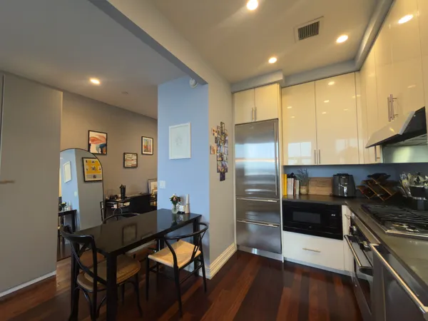 a kitchen with stainless steel appliances kitchen island granite countertop a refrigerator a stove a sink a dining table and chairs with wooden floor