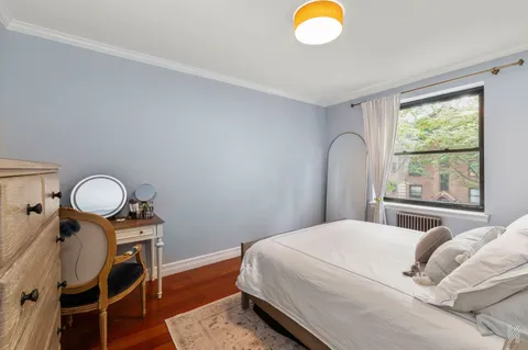 a bedroom with a bed and dresser with wooden floor