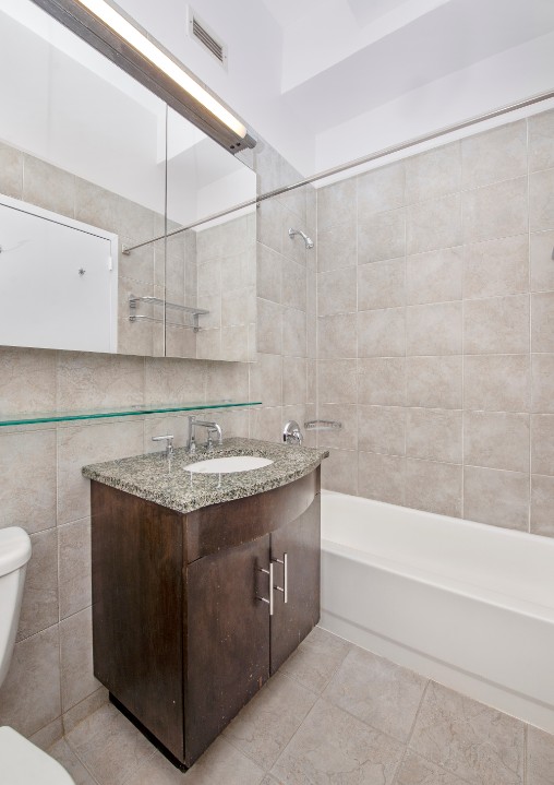 80 John Street, Unit 4C Manhattan, NY 10038 - Photo 9 of 11 a bathroom with a granite countertop sink a toilet and bathtub