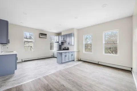 a living room with stainless steel appliances kitchen island granite countertop a stove a sink a refrigerator white cabinets and wooden floor