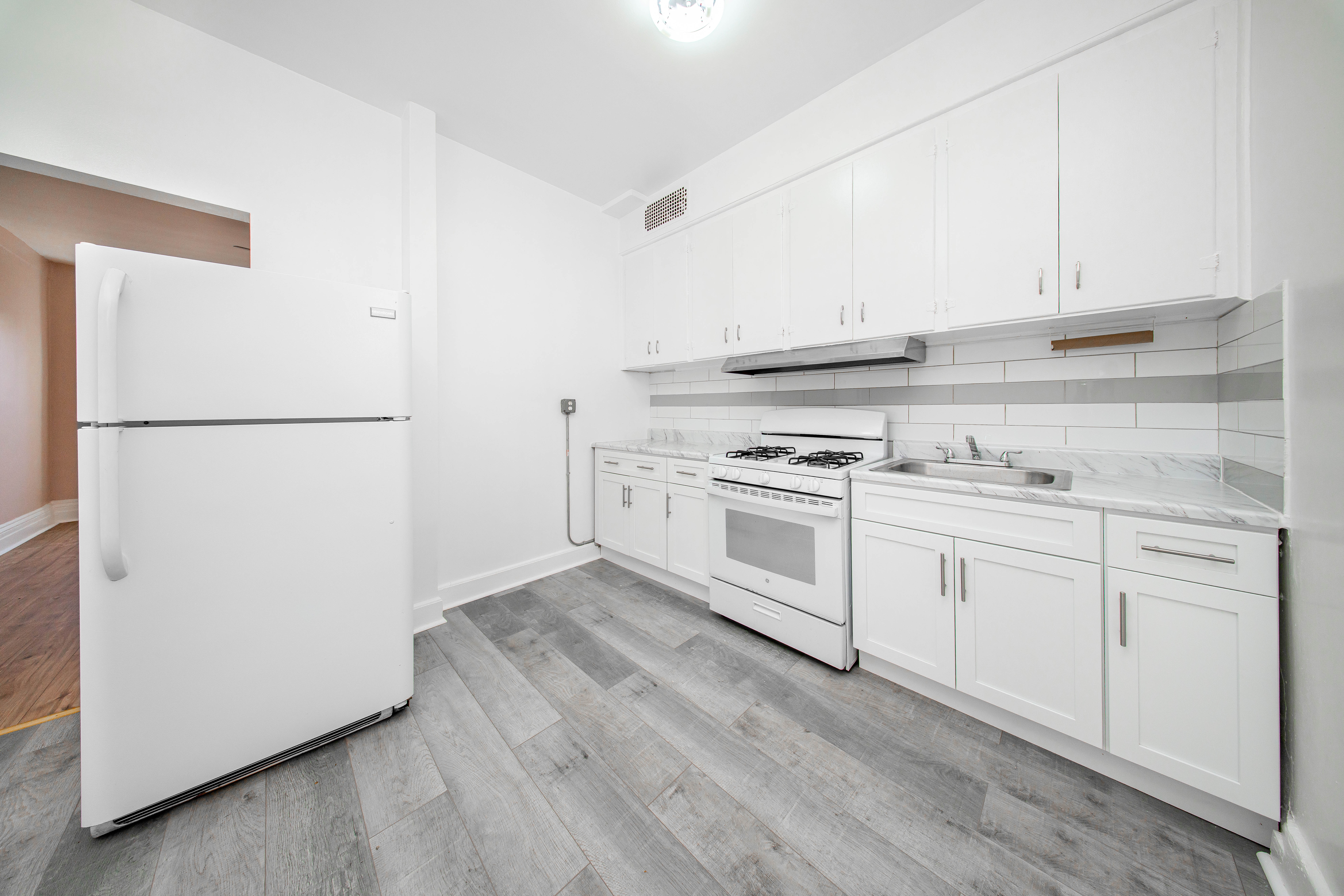 22-17 Astoria Boulevard, Unit 2W Queens, NY 11102 - Photo 6 of 10 a white kitchen with sink and white stainless steel appliances