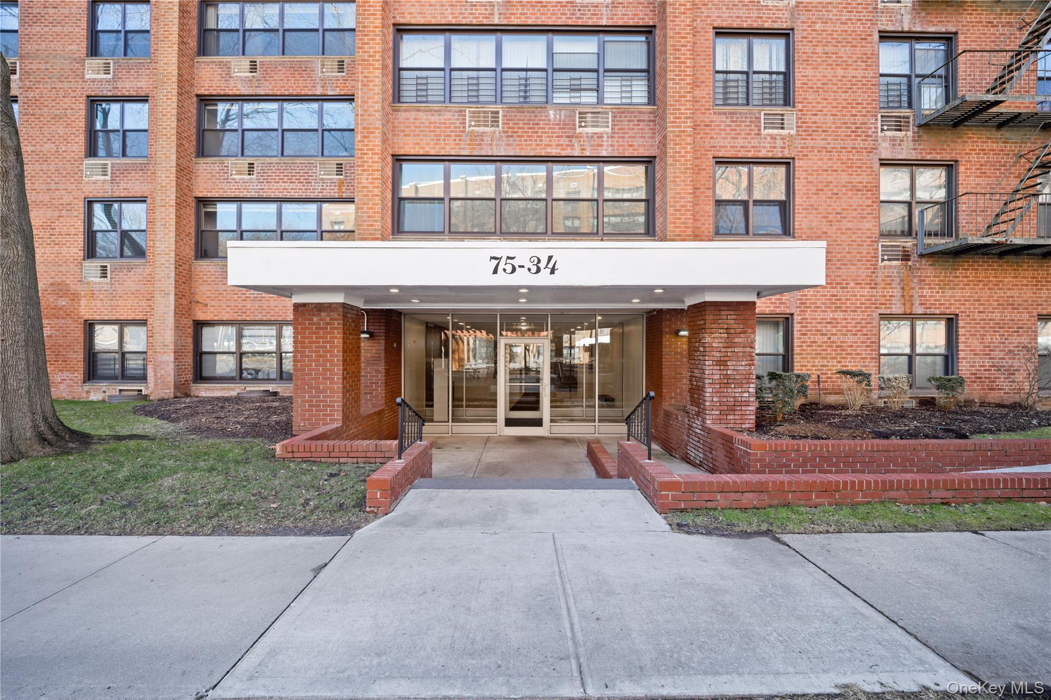 75-34 Bell Boulevard, Unit LD Queens, NY 11364 - Photo 2 of 26 front view of a brick building with a bench in front of building