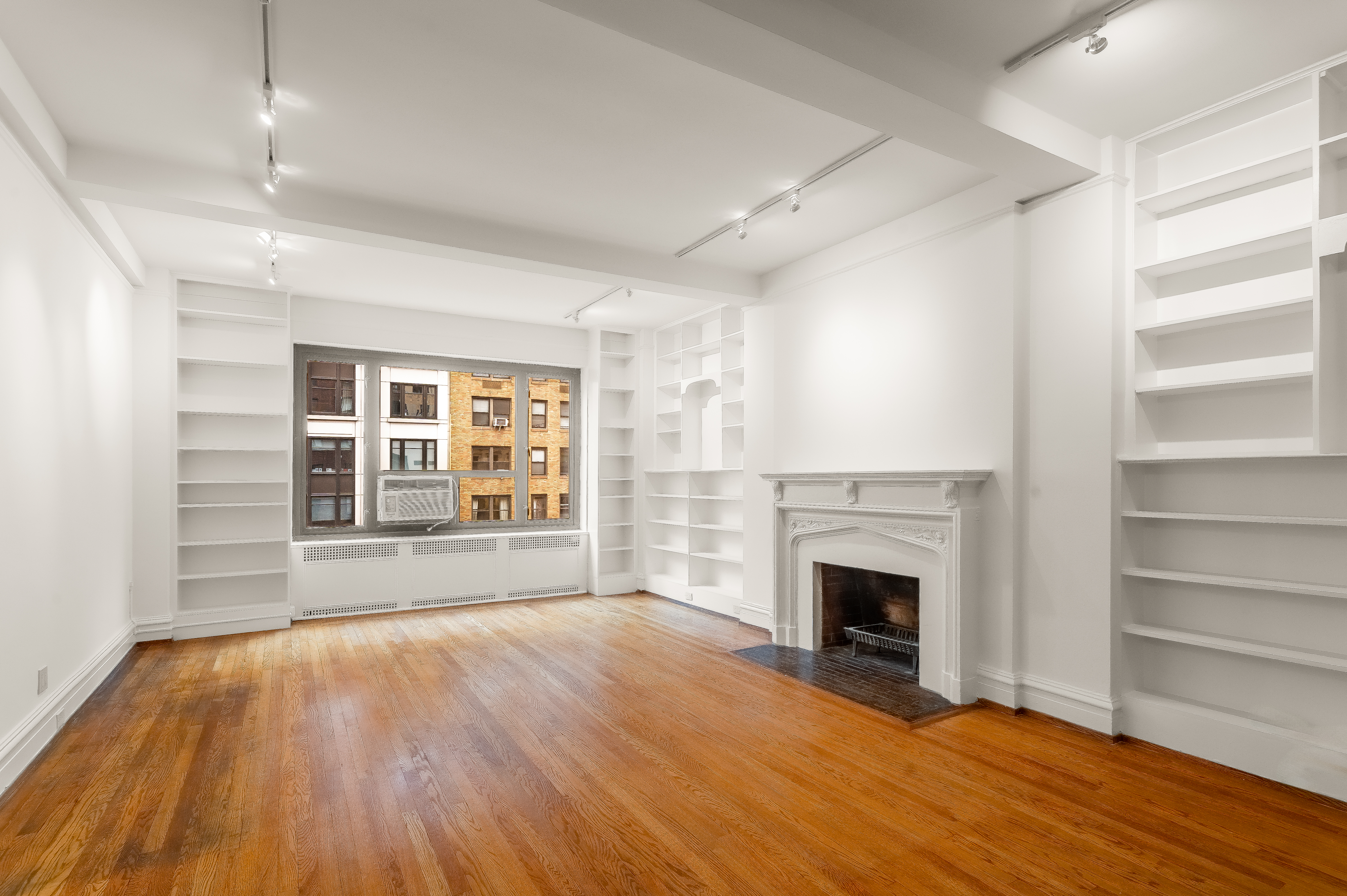 180 East 79th Street, Unit 5A Manhattan, NY 10075 - Photo 5 of 19 a view of an empty room with wooden floor fireplace and a window