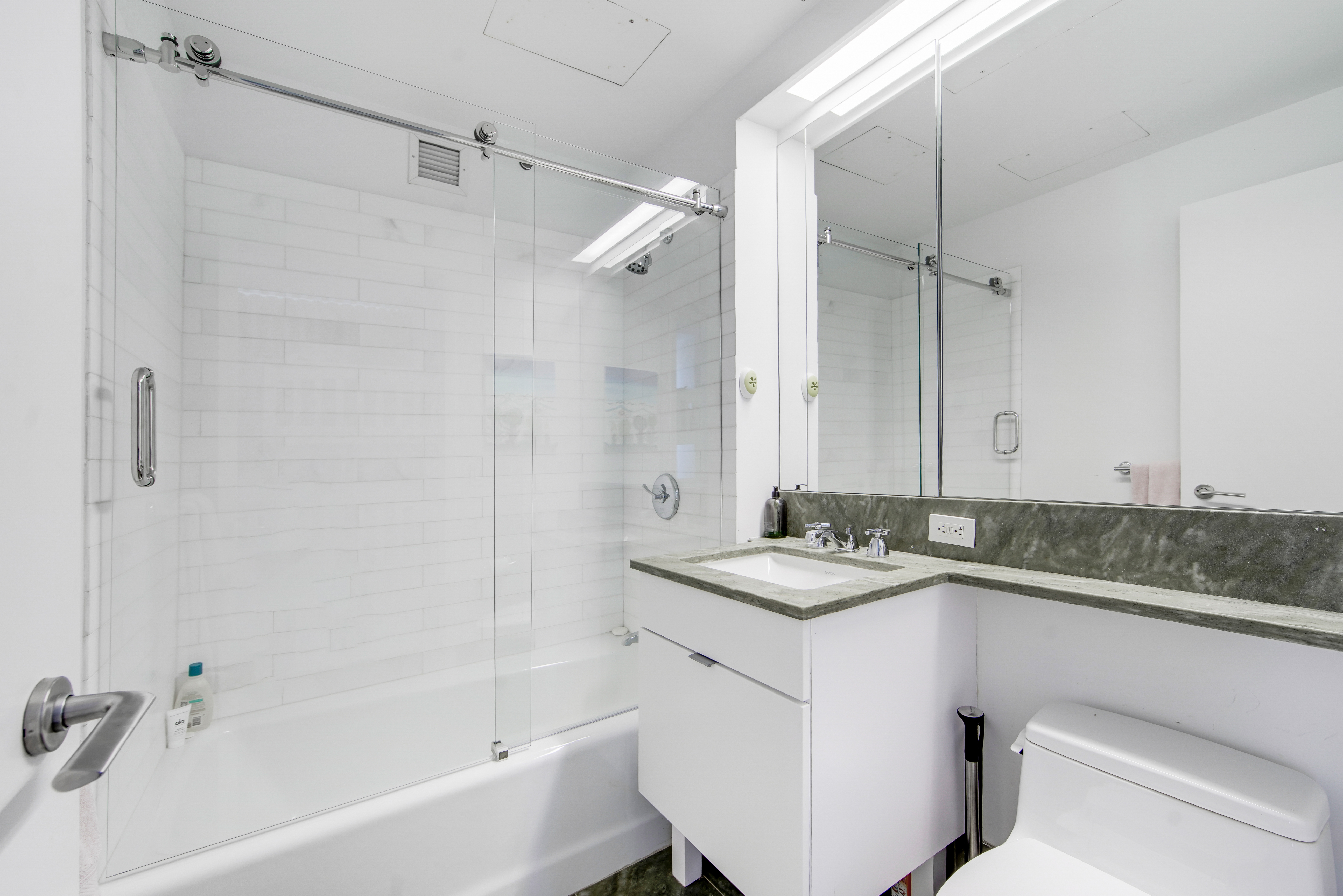 207 East 57th Street, Unit 20A Manhattan, NY 10022 - Photo 15 of 18 a bathroom with a granite countertop sink mirror toilet and bathtub