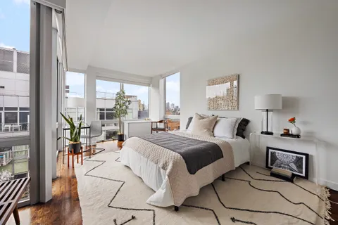 a large bedroom with a bed a large window and walk in closet with wooden floor