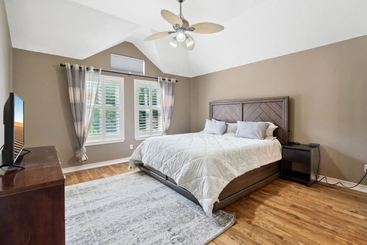 a bedroom with a large bed and a flat tv screen on dresser