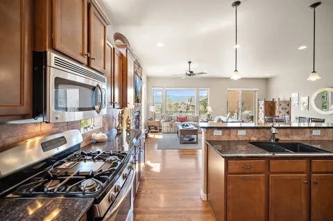 a kitchen with stainless steel appliances kitchen island granite countertop a stove a refrigerator a kitchen island a dining table and chairs with wooden floor