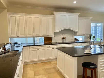 a kitchen with kitchen island granite countertop a sink a stove and white cabinets