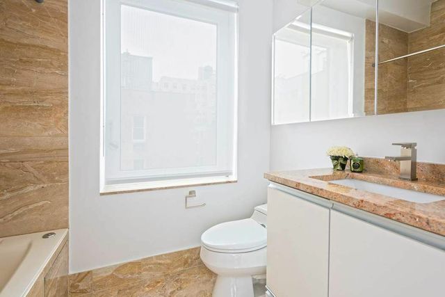 30 East 85th Street, Unit 8B Manhattan, NY 10028 - Photo 7 of 12 a bathroom with a granite countertop sink toilet and a mirror