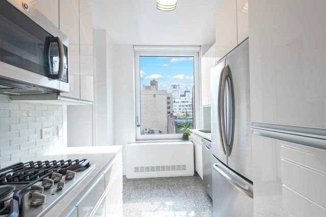 30 East 85th Street, Unit 8B Manhattan, NY 10028 - Photo 4 of 12 a kitchen with stainless steel appliances a refrigerator a sink and wooden cabinets