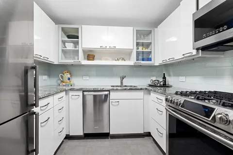 a white kitchen with stainless steel appliances granite countertop a stove and a sink
