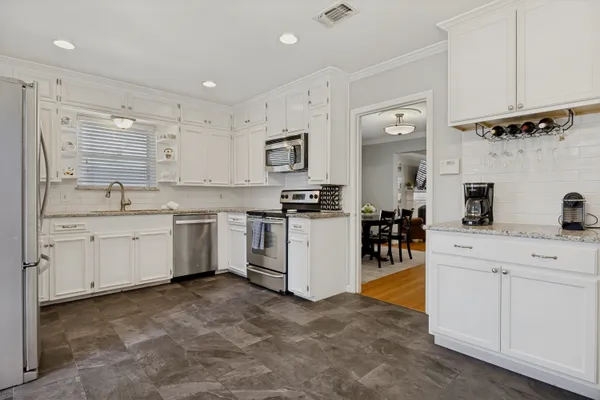a kitchen that has a lot of white cabinets and stainless steel appliances