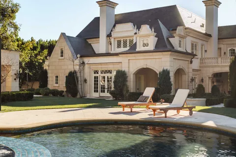 a view of a brick house with small yard plants and palm trees