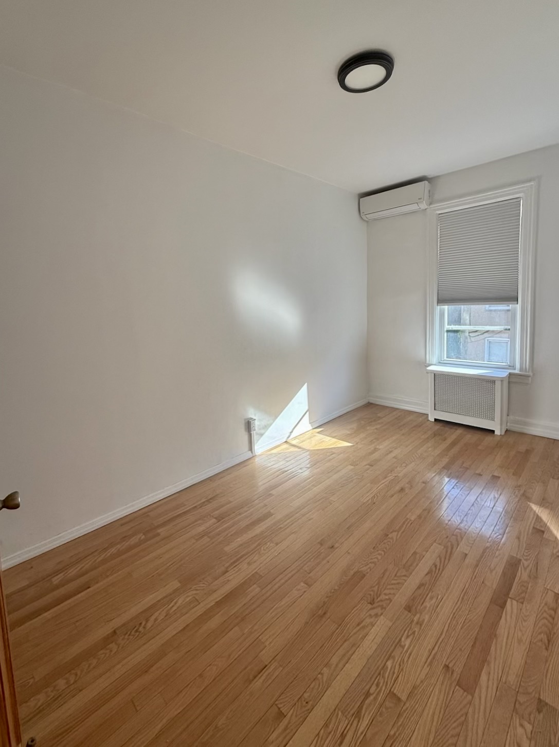 18-48 21st Drive, Unit 1R Queens, NY 11105 - Photo 3 of 11 an empty room with wooden floor and windows
