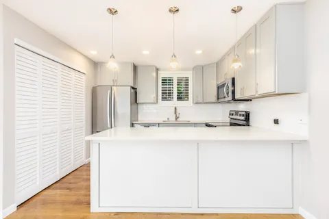 a kitchen with stainless steel appliances granite countertop a sink a oven a refrigerator and white cabinets with wooden floor