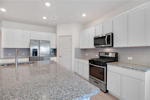 a kitchen with granite countertop a stove top oven a sink a counter space and cabinets