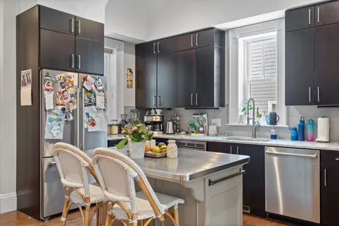 a kitchen with stainless steel appliances a sink a stove a refrigerator cabinets and a dining table