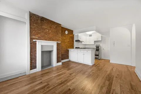 a view of an empty room with wooden floor and a kitchen
