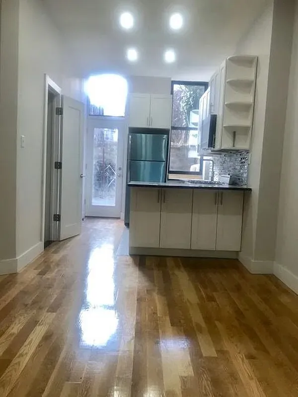 a view of an empty room with wooden floor and a kitchen