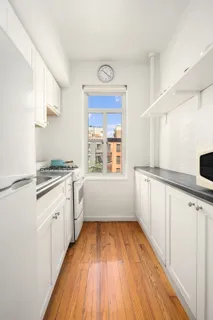 a kitchen with granite countertop a stove a sink and white cabinets with wooden floor