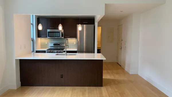 a living room with stainless steel appliances wooden floor and view kitchen