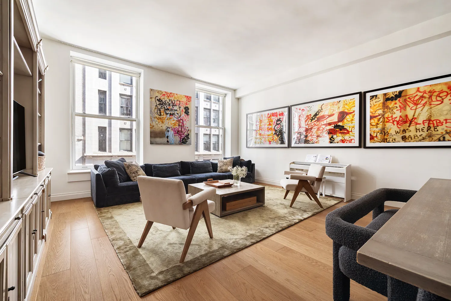 a living room with furniture two large window and wooden floor