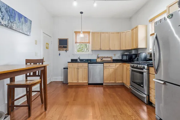 a kitchen with stainless steel appliances a stove a sink dishwasher a refrigerator white cabinets and wooden floor